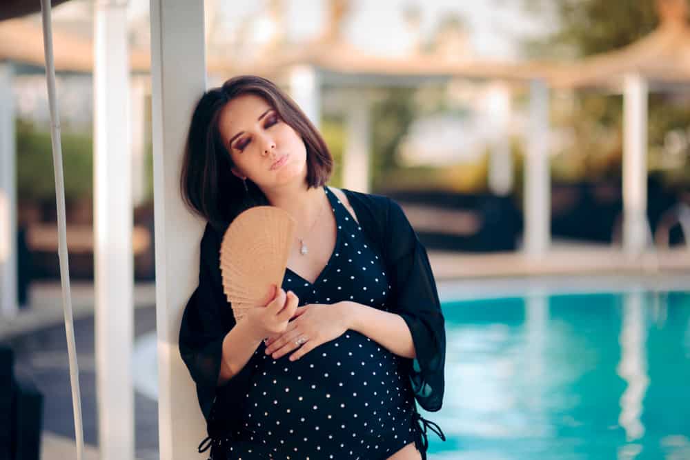 一位身著泳衣、受熱折磨的游泳池旁的孕婦