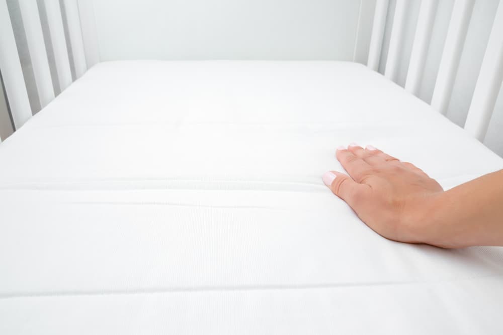 一個女人的手壓在嬰兒床床墊上